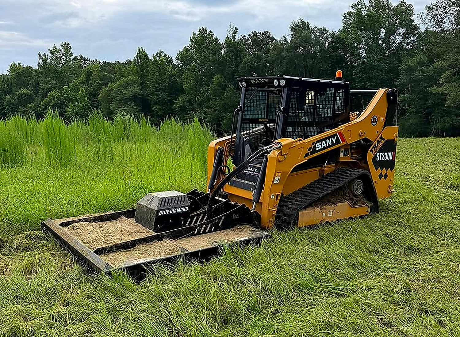 SANY track loader with a brush cutter attachment standing in tall uncut grass