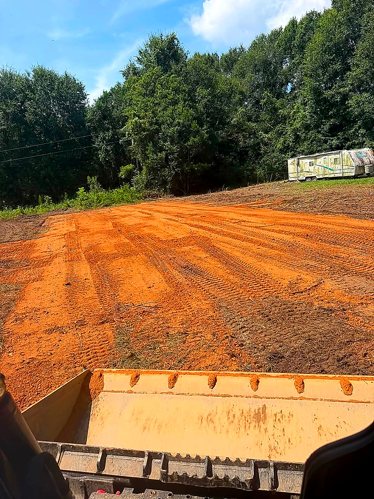 A wide fresh red-clay pad seen over the tailgate of the dump trailer