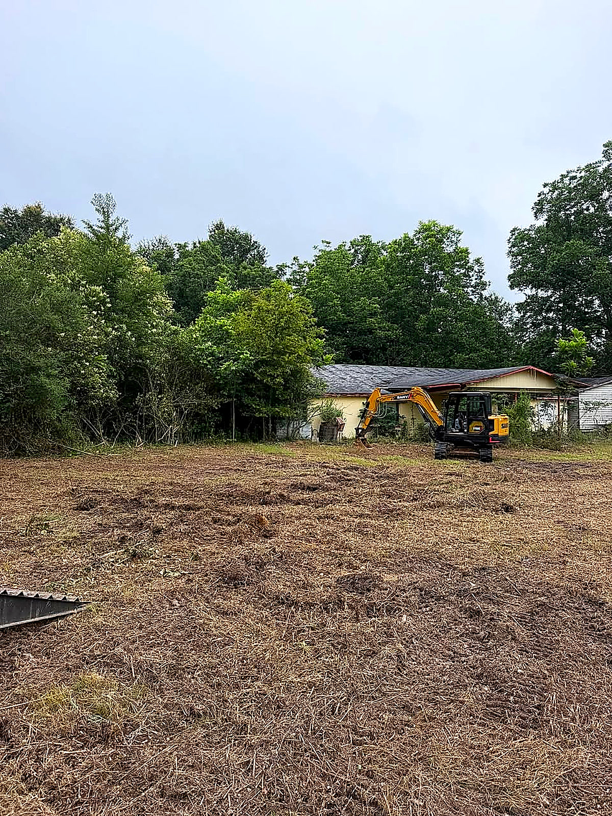 A cleared building lot with an excavator working near the house at the back