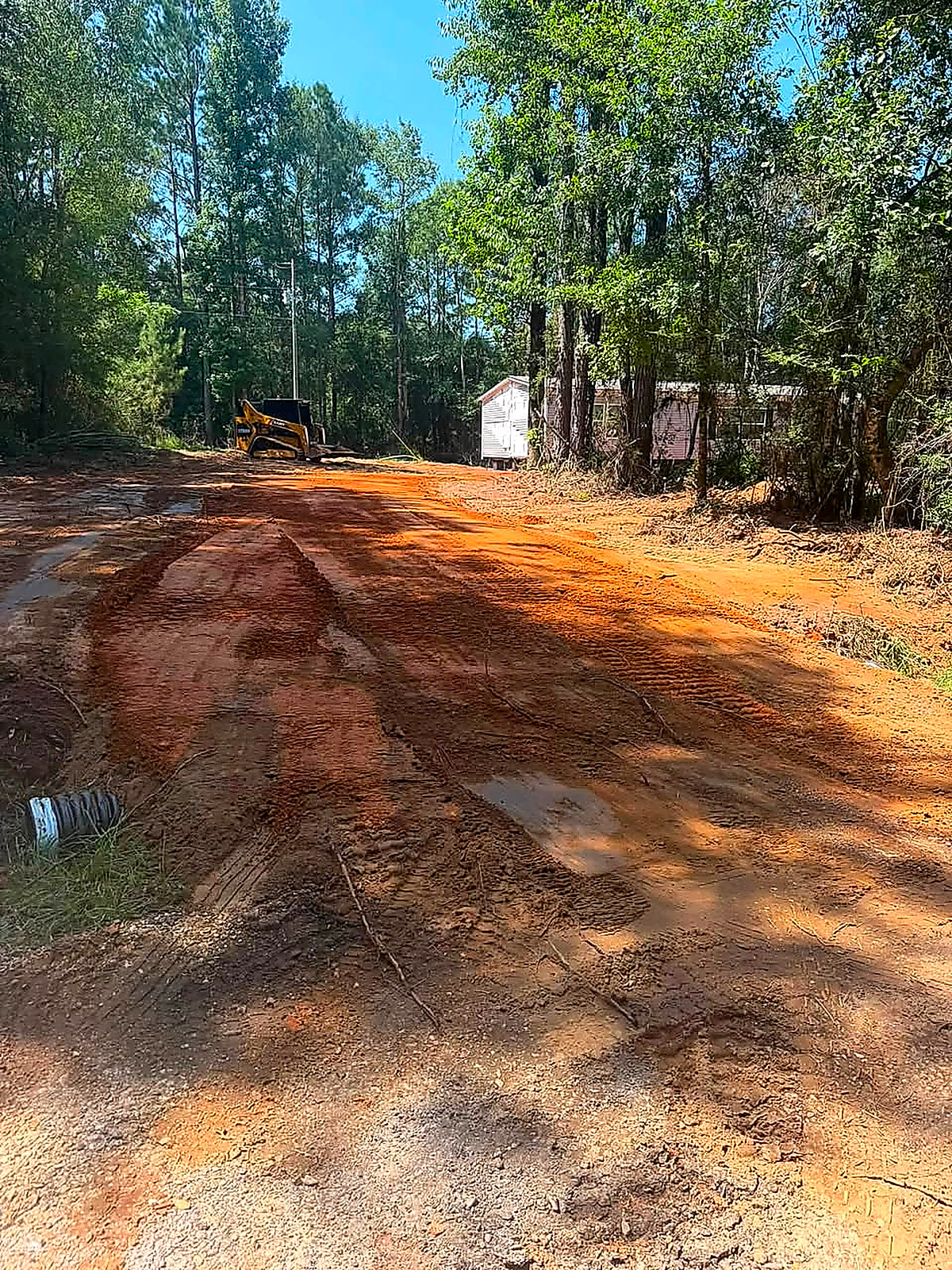 A new red-dirt driveway curving up toward a mobile home with the machine still on site