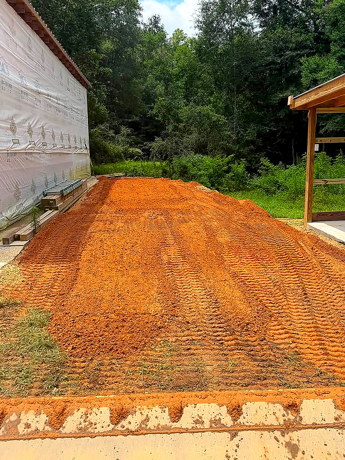 A built-up red-dirt pad beside a building, seen over the tailgate of the dump trailer
