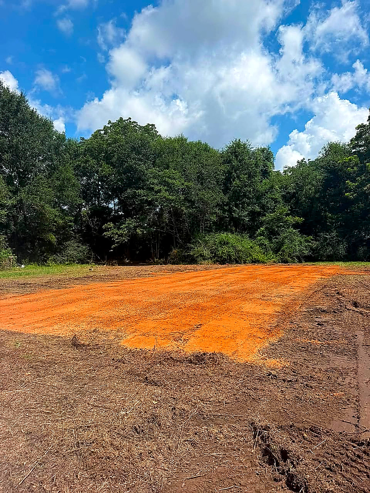 A wide red-dirt pad graded out in an open yard under a blue sky