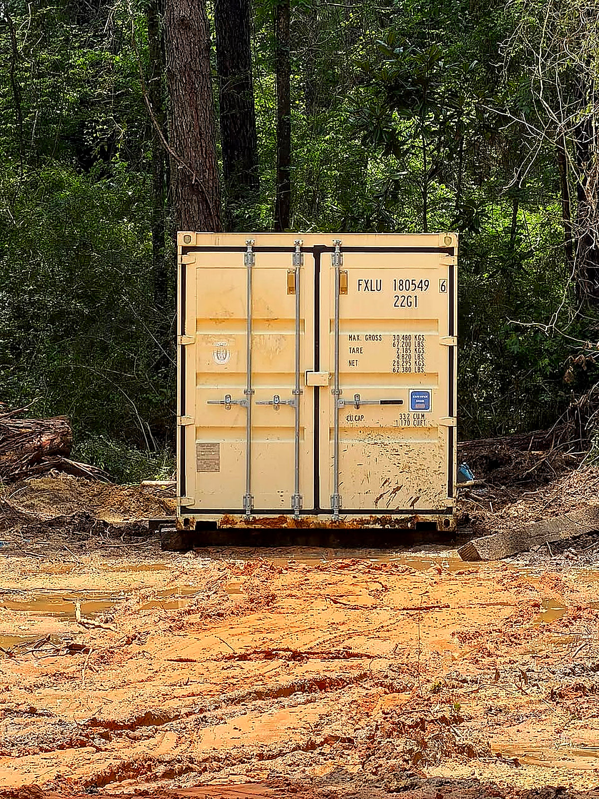 A shipping container set and levelled on fresh red dirt among the pines
