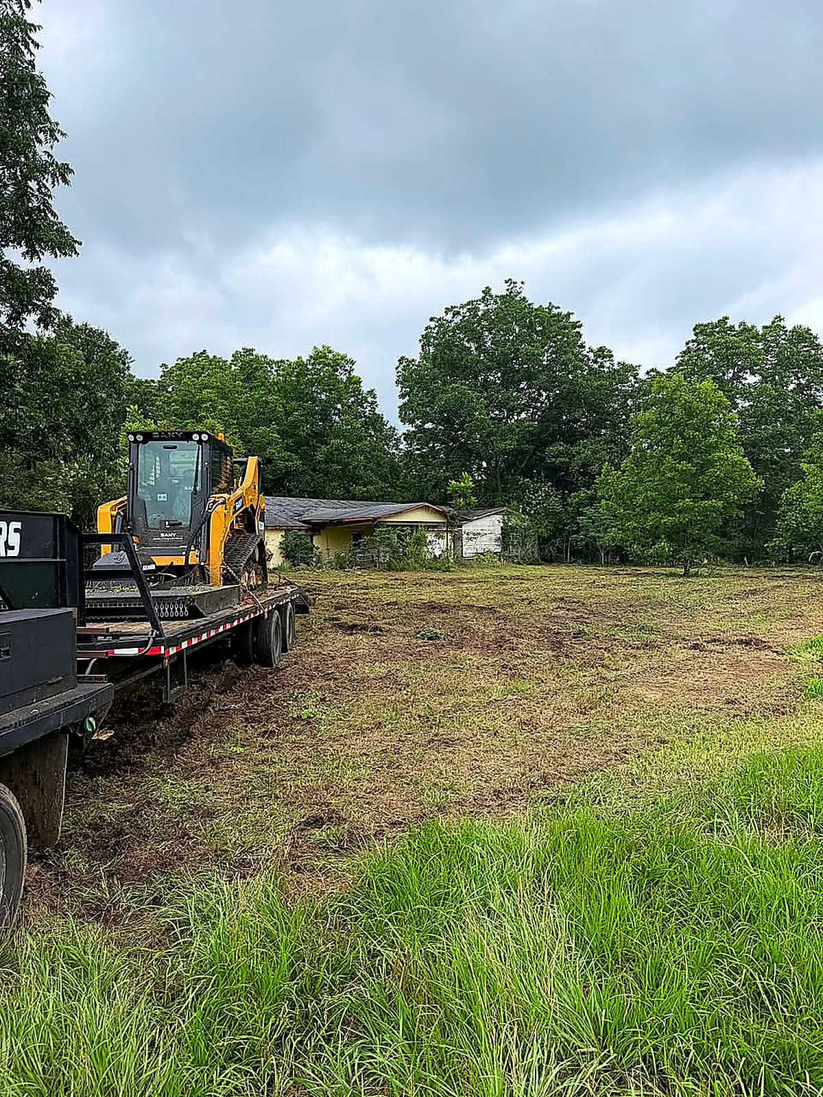 The track loader loaded on the trailer beside a field with a barn behind it