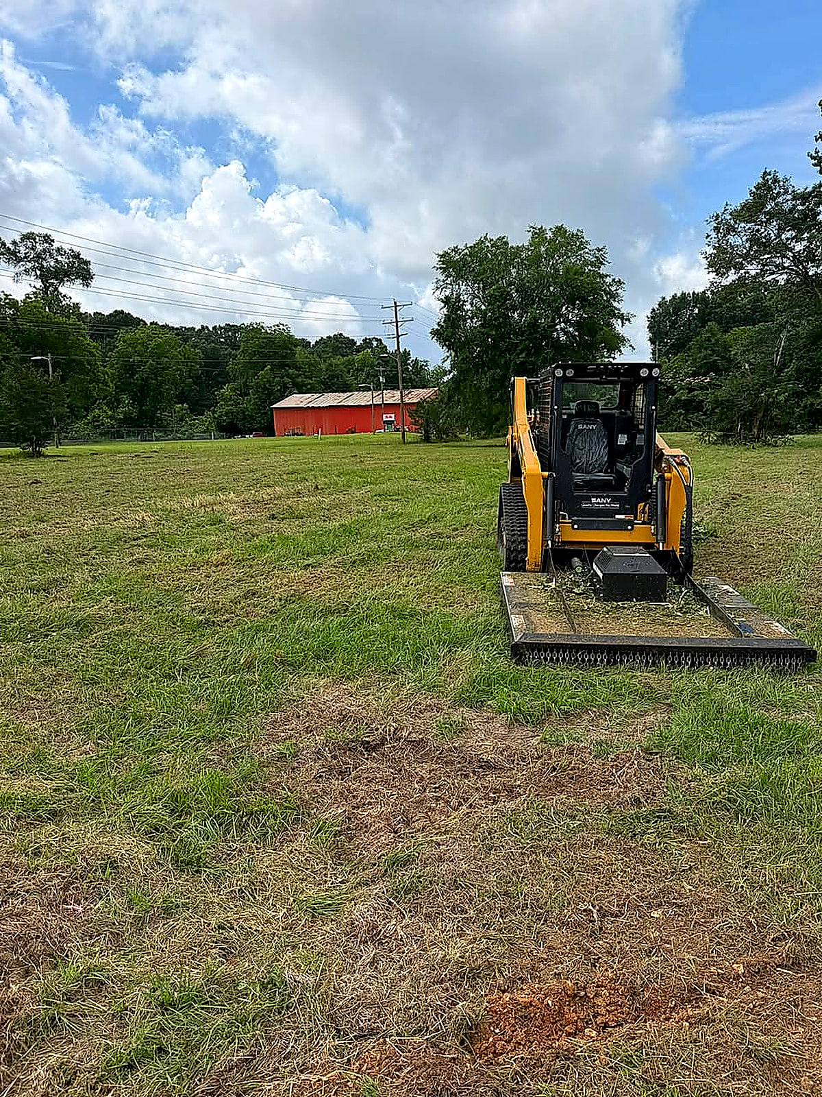Track loader working an open green field with a red barn in the background