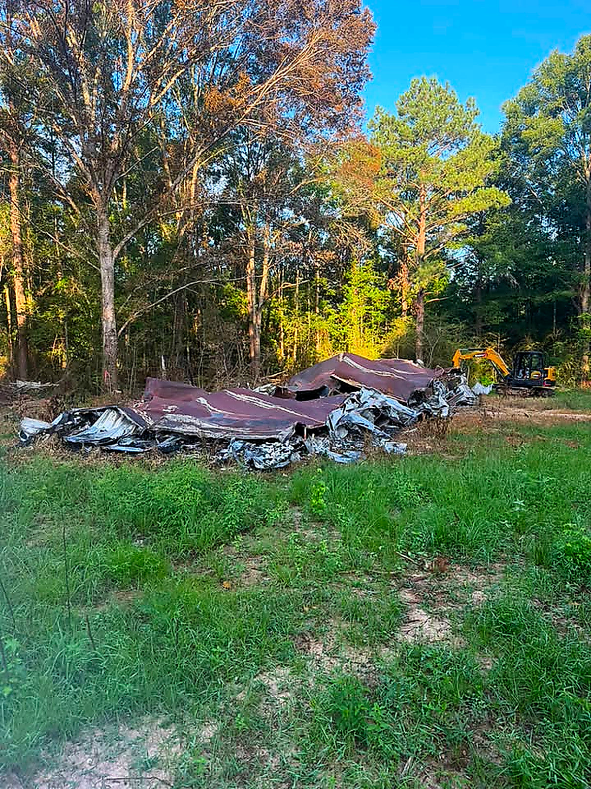 A pile of burnt mobile home debris and twisted metal lying in a green field